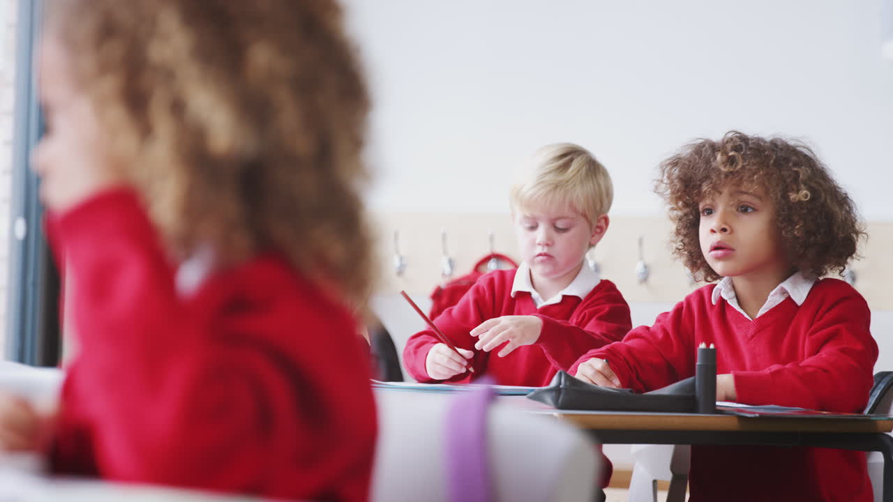 jóvenes escolares en uniforme escolar dibujando en el escritorio en una clase de escuela infantil, de cerca