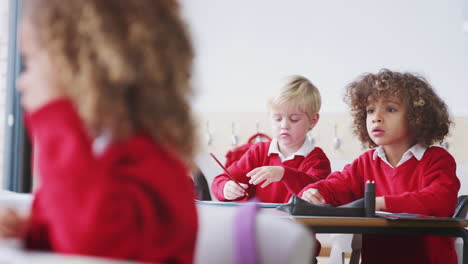 young schoolboys in school uniform drawing at desk in an infant school class, close up