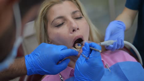 orthodontist uses mouth mirror to inspect blonde woman's teeth at dental clinic dentist patient