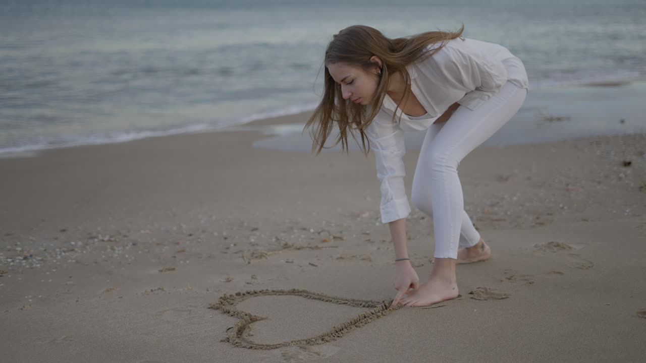 Woman Drawing a Heart in the Sand on the Beach