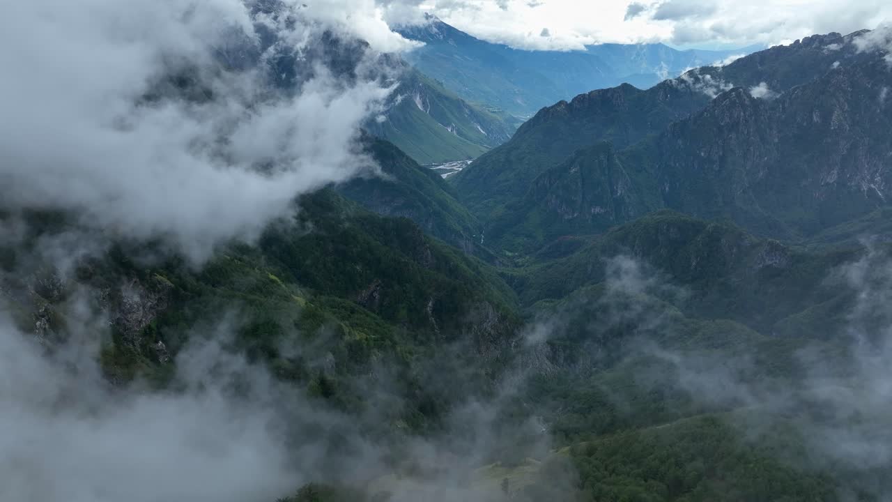 Mist clouds reveals lush green mountain peaks in Theth, Albania, aerial fly through establishing
