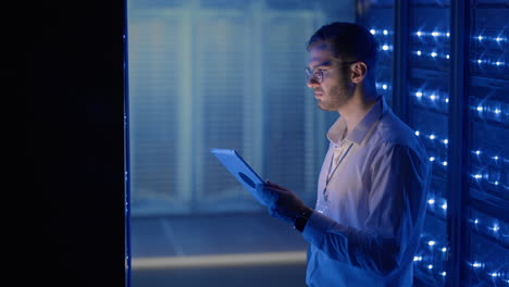 it technician in data center digital server room controlling work of rack server cabinets with a tablet. professional server engineer at work.