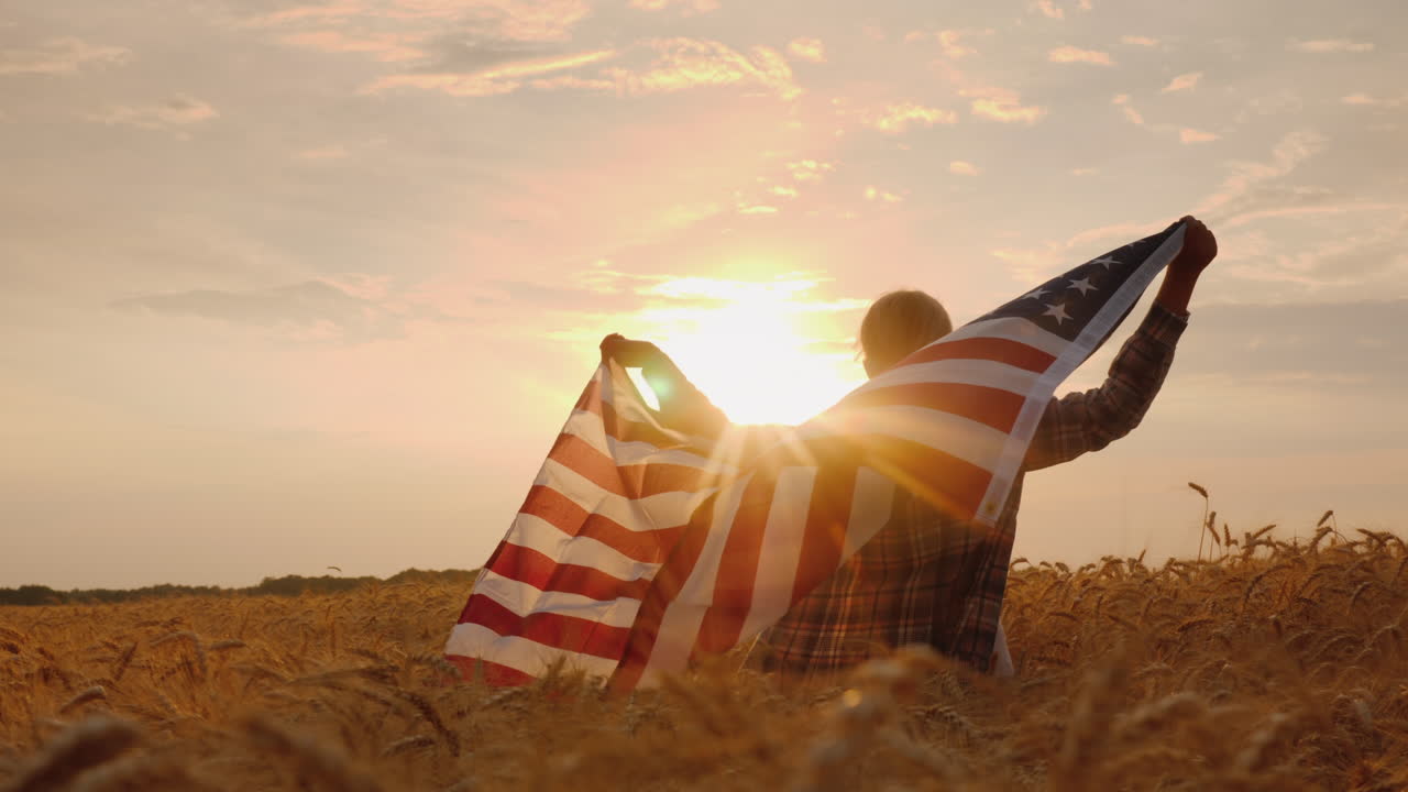 一名男子拿着美国国旗站在风景如画的小麦田中