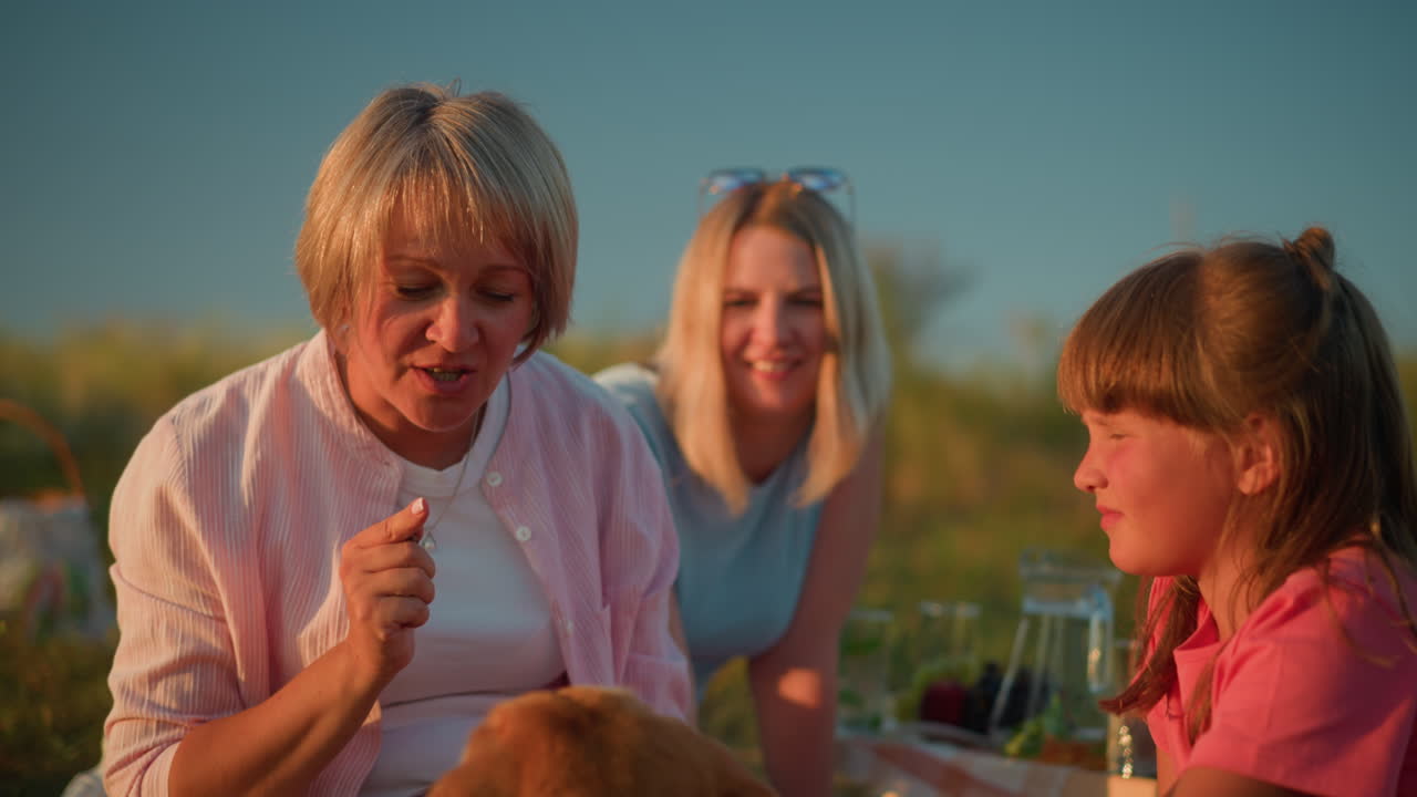 Animal trainer instructs her dog to kiss while smiling friend watches in background and little girl observes, trainer gestures to dog with affection, creating an engaging moment of pet