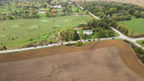 aerial orbital view of car traffic accident incident site at countryside rural road, first aid vehicles fire trucks and stationary cars along the street roadside, green golf field and lands around