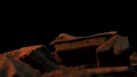 slow motion static shot of falling chocolate pieces in cocoa while the ground rotates against a black background