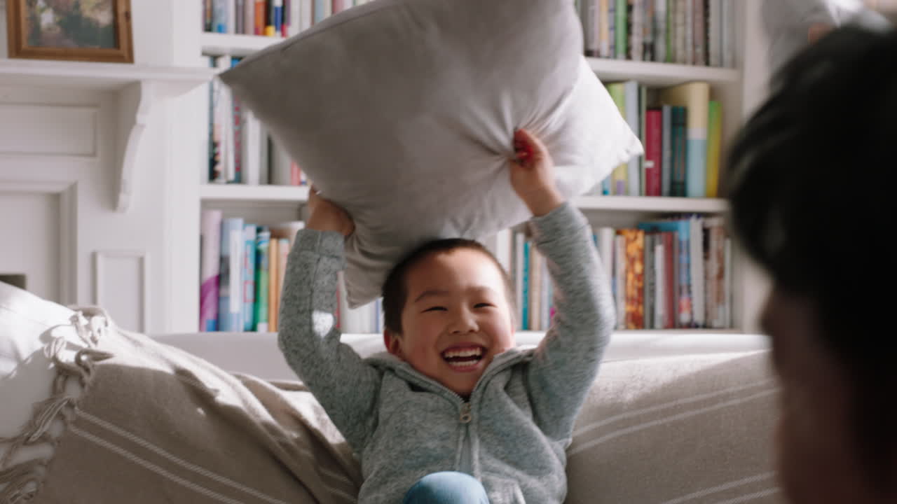 happy asian family having pillow fight mother and father enjoying playing with children at home having fun together on weekend 4k footage