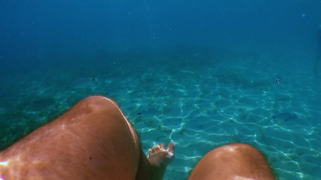 수면 아래에 있는 맑고 투명한 바닷물에 떠 있는 사람 다리의 개인적인 관점에서 느린 동작