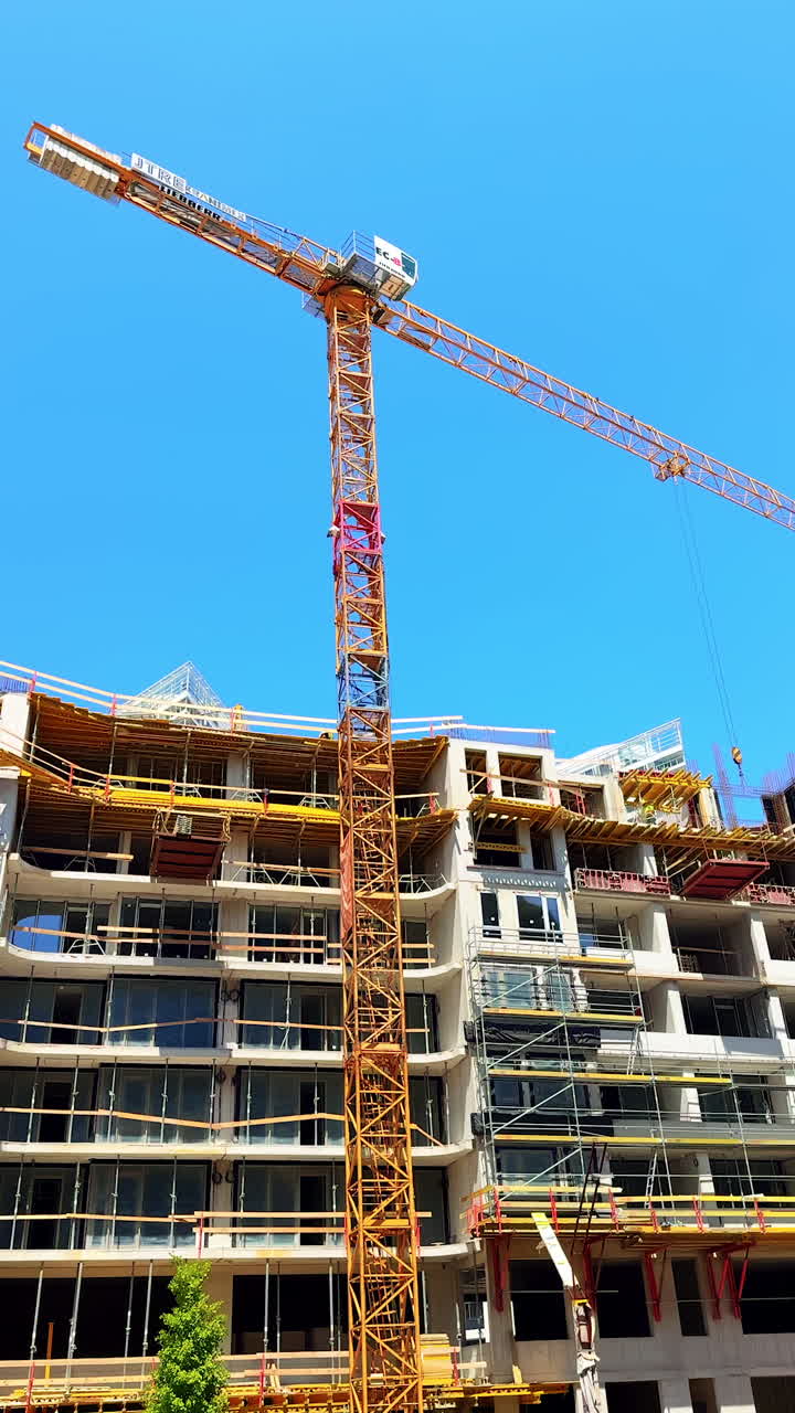 Construction gear at site. Tower crane operates above a multi-story building under construction in bright, clear blue sky on a sunny day