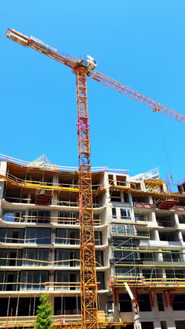 construction gear at site. tower crane operates above a multi-story building under construction in bright, clear blue sky on a sunny day