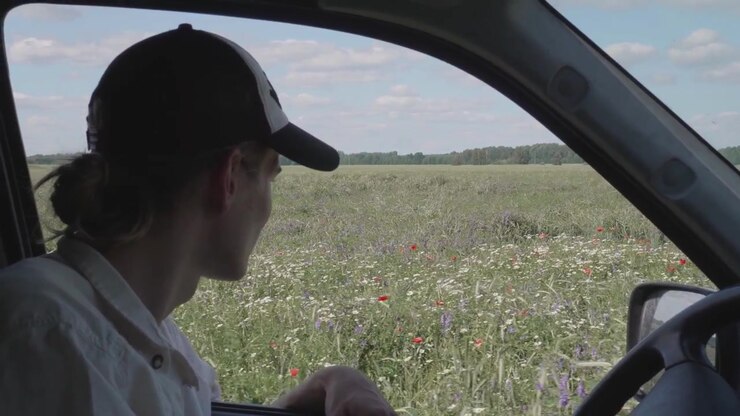 White man with a baseball cap driving by a meadow