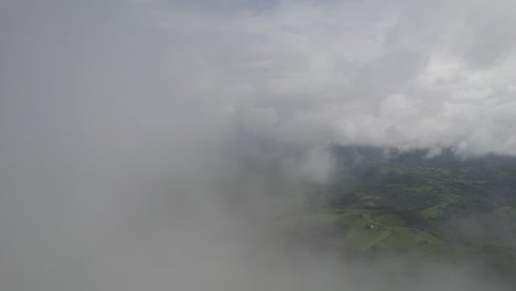 Lush-forest-peeking-through-white-clouds,-creating-a-serene-atmosphere,-aerial-view