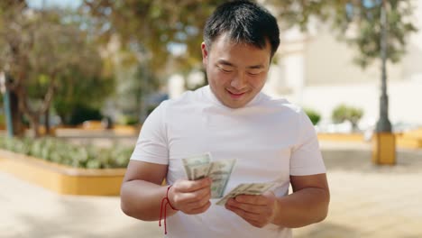 young chinese man smiling confident counting dollars at park