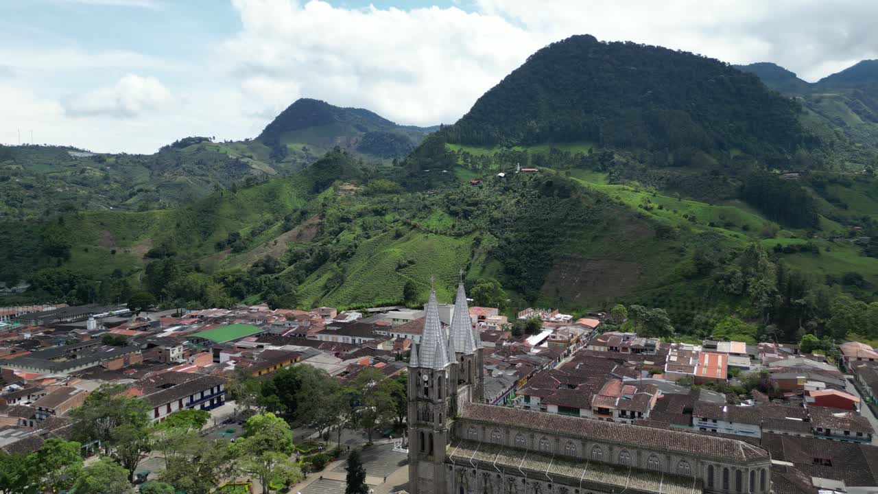 Aerial drone footage of the picturesque Andean town of Jardín in Colombia, featuring the central square, the church Basílica Menor de la Inmaculada Concepción and the surrounding mountain landscape