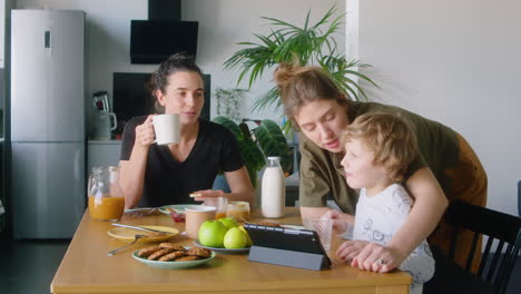 lesbian mother and kid using tablet at home breakfast