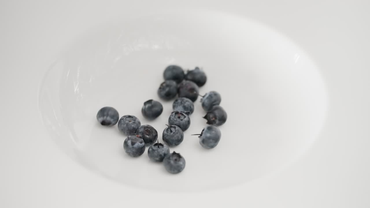 Extreme close-up shot of fresh, organic blueberries falling and tumbling in slow motion into a clean white bowl, perfect for concepts of healthy eating, diet, vitamins, and nutritious food.