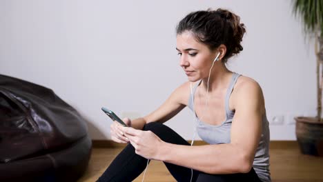 Smiling-sportswoman-watching-video-lesson-on-smartphone-at-home