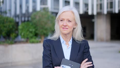thoughtful senior businesswoman in suit holding technology outdoors