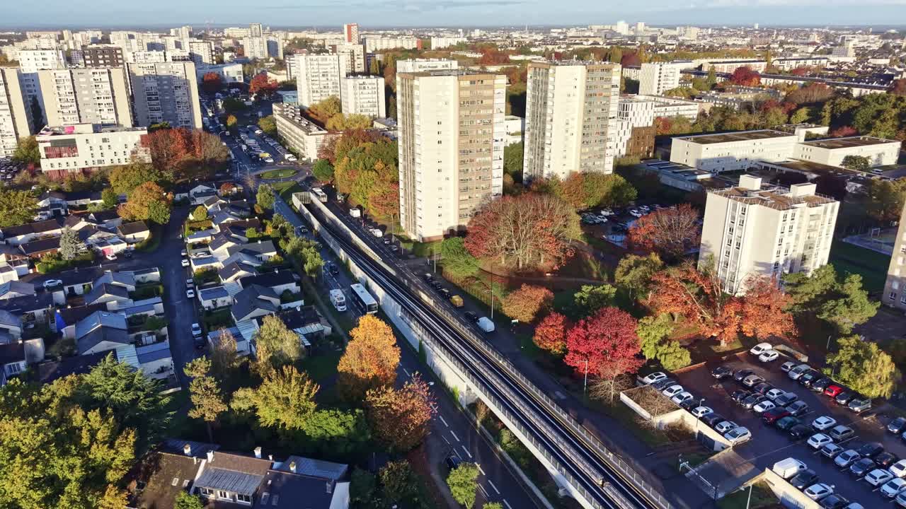 Drone flying above La Poterie metro station in Rennes on a sunny day, showing the elevated tracks, nearby roads with buses and cars, parking lots and residential buildings