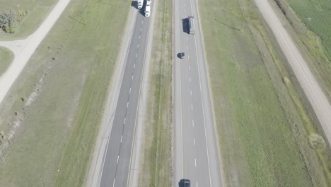 aerial birds eye view dolly roll over a the interstate highway as theres a grass field divider between 2 lanes on each side headed east or west or north or south on a sunny summer day by farms hwy2-2