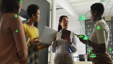 Animation-of-globes-of-digital-icons-against-group-of-diverse-women-discussing-together-at-office