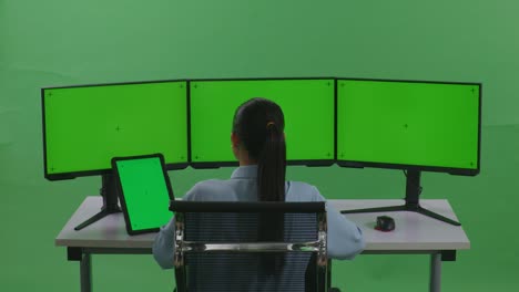 woman working at a multi-monitor workstation on a green screen