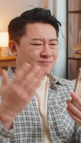 화가 난 중국인 남자가 스마트폰을 이용해 안 좋은 소식을 읽으며 거실에 있는 소파에 앉아 있다.
