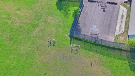 small group of people playing soccer on green grassy football field in park playground, aerial top down view