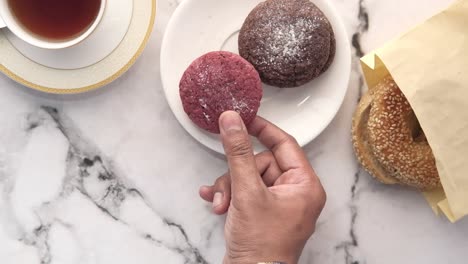 hand holding a cookie with tea and other baked goods on the table