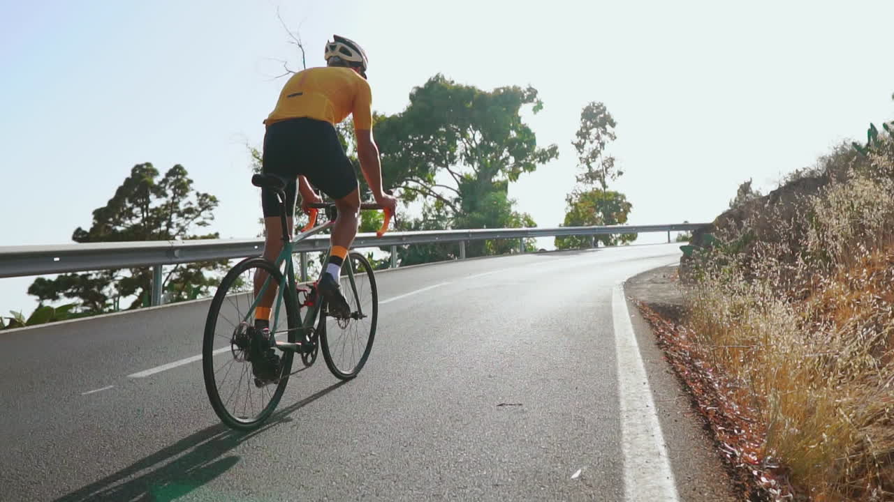 Pedaling his road bike, a man engages in outdoor exercise on a quiet morning road. The slow-motion footage captures the essence of extreme sports