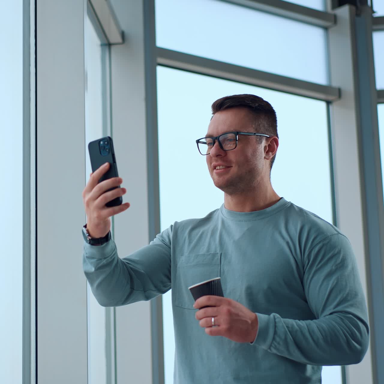 Relaxed businessman with a cup in his hand having lunch break. Man is looking at phone taking video or having video conversation