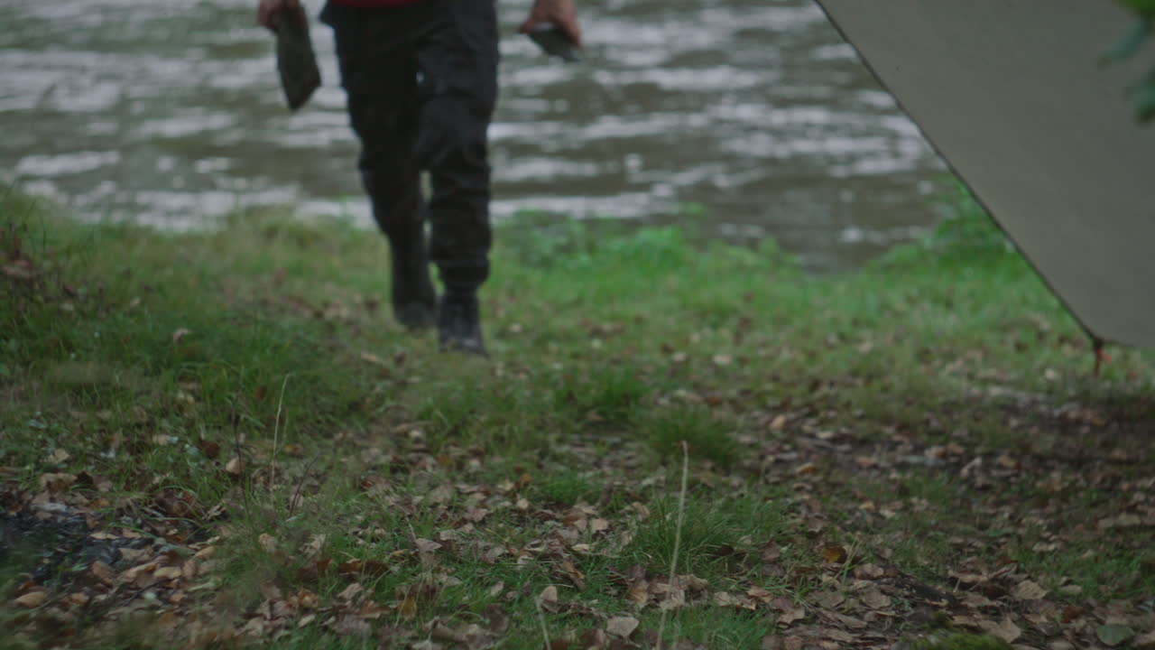Man Placing Rocks on Ground for Securing Tent on Riverbank
