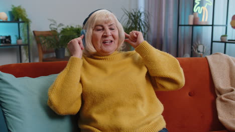 happy grandmother woman in wireless headphones relaxing on sofa at home listening favorite music