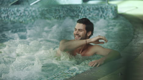 joyful man resting in whirlpool bath. smiling man saying hi at spa hotel.