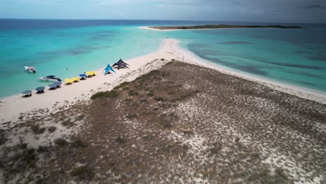 a sandy beach and turquoise waters with boats and tents on a sunny day, aerial view