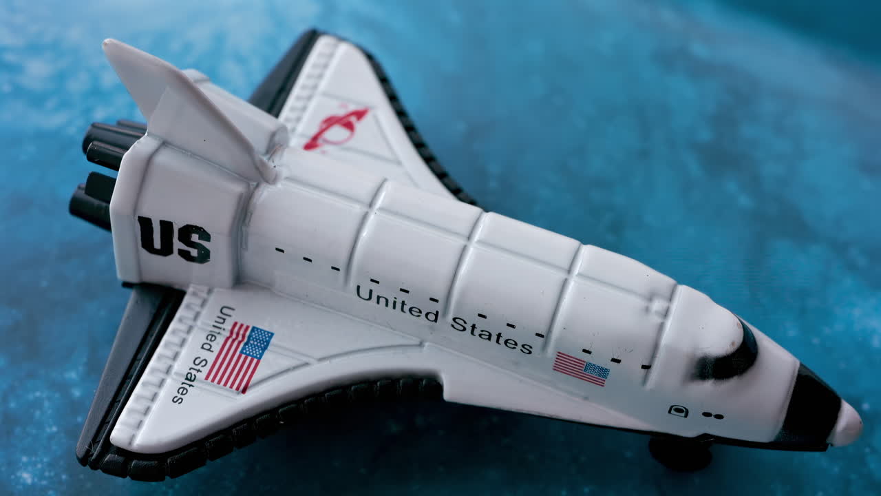 Close up of a miniature toy space shuttle placed on a blue cosmic galaxy backdrop