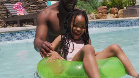 Feliz-Padre-E-Hija-Afroamericanos-Divirtiéndose-En-La-Piscina-Con-Anillo-Inflable