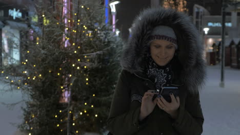 woman using mobile walking in the street with christmas decorations