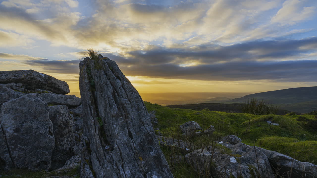 Timelapse of rural nature landscape with ruins of prehistoric passage tomb in the foreground during dramatic sunset viewed from Carrowkeel in county Sligo in Ireland