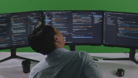 back view of asian man developer having backache while write code with multiple computer screens in green screen studio