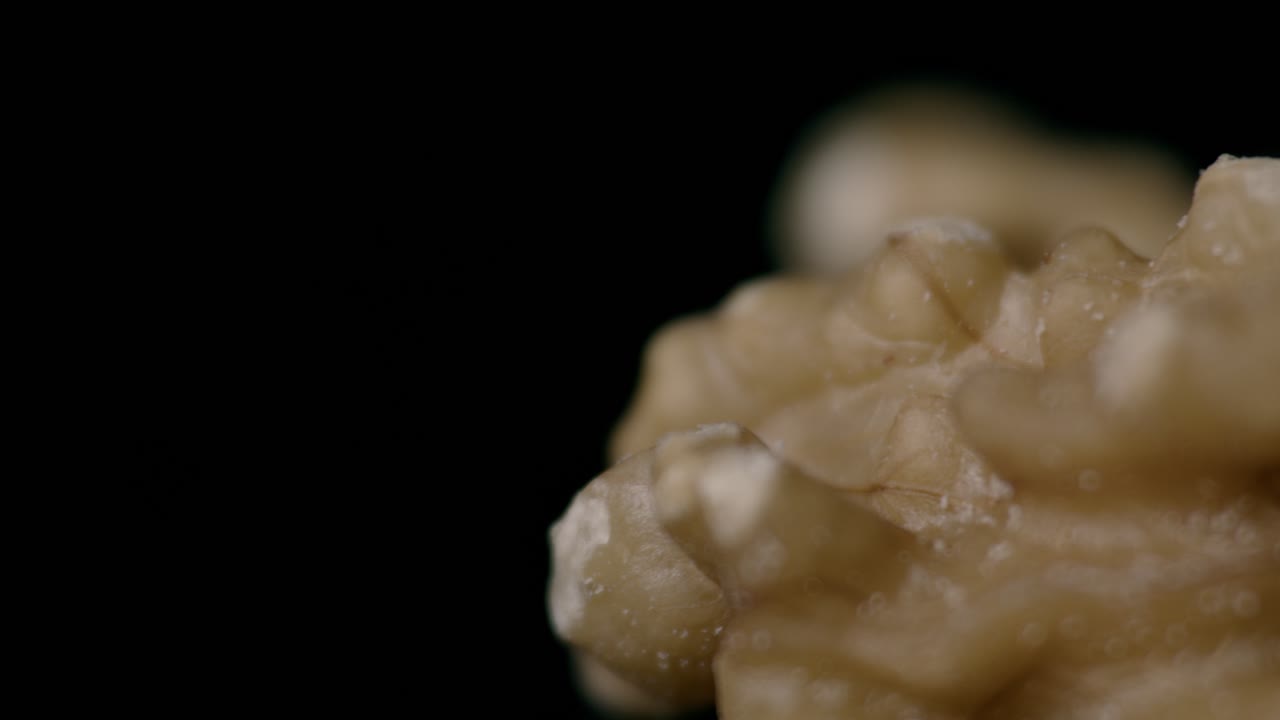 A detailed close-up of assorted nuts—such as almonds, walnuts, cashews, and hazelnuts—displayed against a dark background. The moody lighting emphasizes texture, color, and natural form