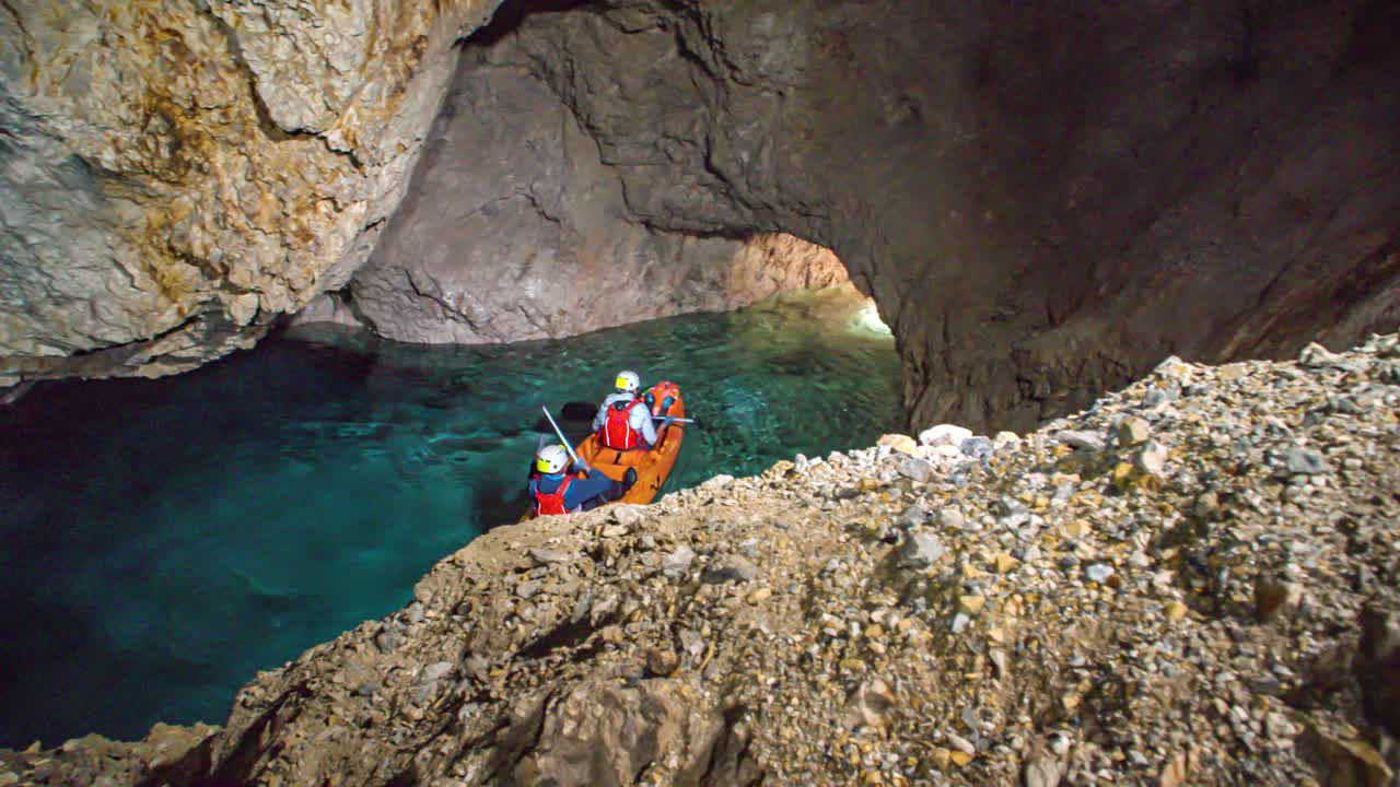 Boys on kayak paddling inside underground mine tunnel, dark rocky cave