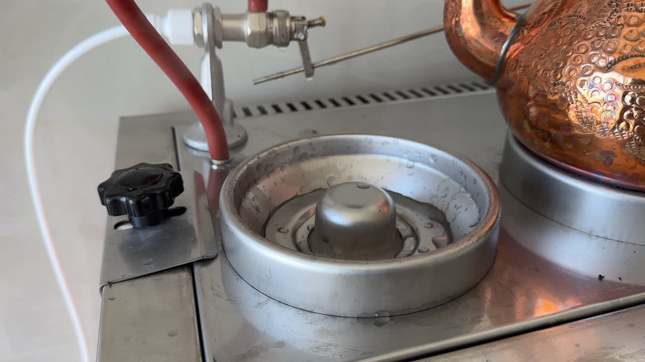Detailed close-up of an industrial tea boiler base with a copper teapot and metal heating element, showing kitchen equipment in use