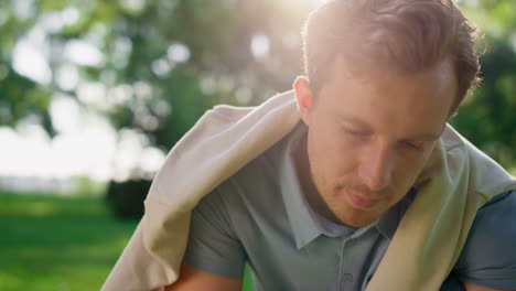 Closeup-happy-blond-man-look-down-in-park.-Handsome-guy-pose-in-golden-sunlight