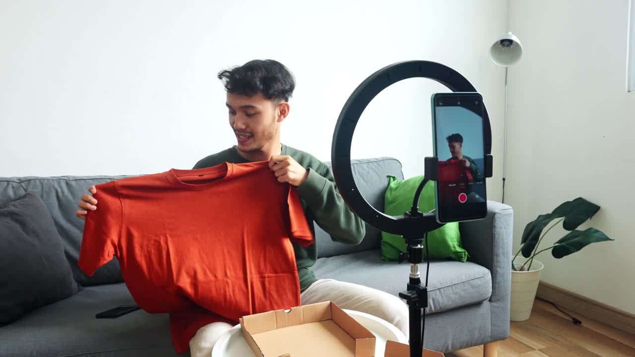 Young Man Presenting t-shirt To Smartphone Camera For Online Product Review Or Sale