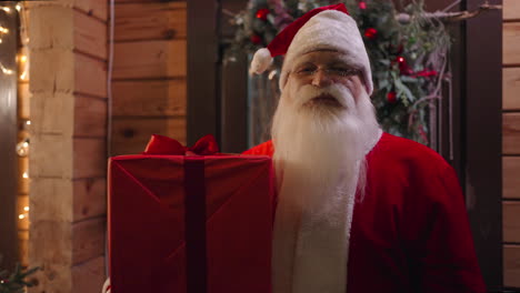 Santa-Claus-looks-into-the-camera-and-enters-the-house-to-leave-gifts-under-the-Christmas-tree-in-winter-in-December-the-camera-moves-away-from-the-portrait-to-the-general-plan