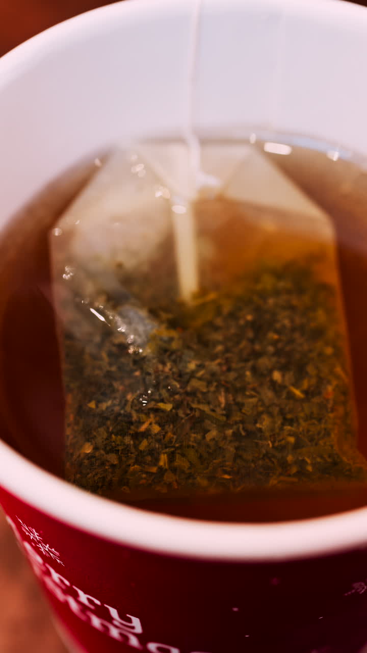Close up of a tea bag brewing into a red cup with Merry Christmas writing on it. Vertical