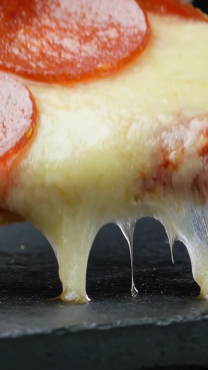 Video verticale: Sollevamento di una pizza ai peperoni mentre una mano afferra la crosta tirando il formaggio fuso su un piatto di ardesia.
