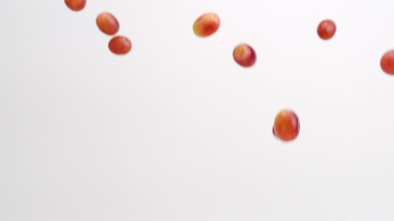 uvas rojas regordetas de la vid lloviendo sobre fondo blanco en cámara lenta