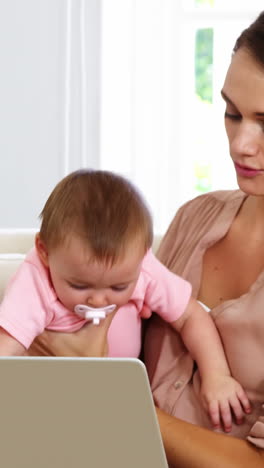 madre linda sosteniendo a su bebé y usando una computadora portátil